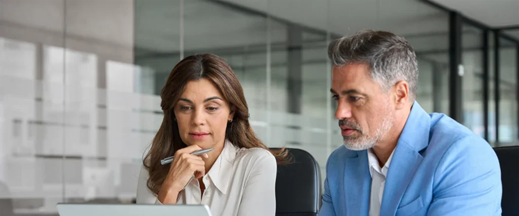 Two business professionals review information on a laptop computer.