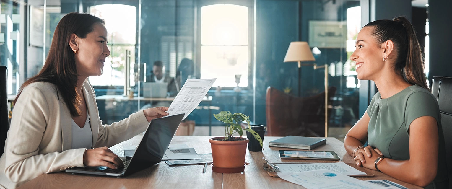 Two people discussing business documents across a table in a shared workspace.
