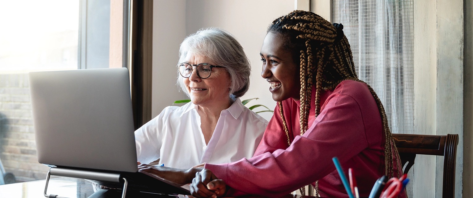 A caregiver and senior citizen at a laptop.